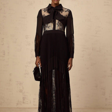 A black maxi dress with floral lace panels and pleated design featuring a long flowing skirt
