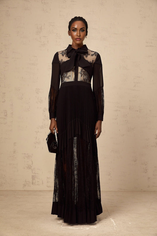 A black maxi dress with floral lace panels and pleated design featuring a long flowing skirt