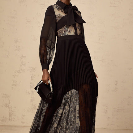 A black maxi dress with floral lace panels and pleated details named Segolene