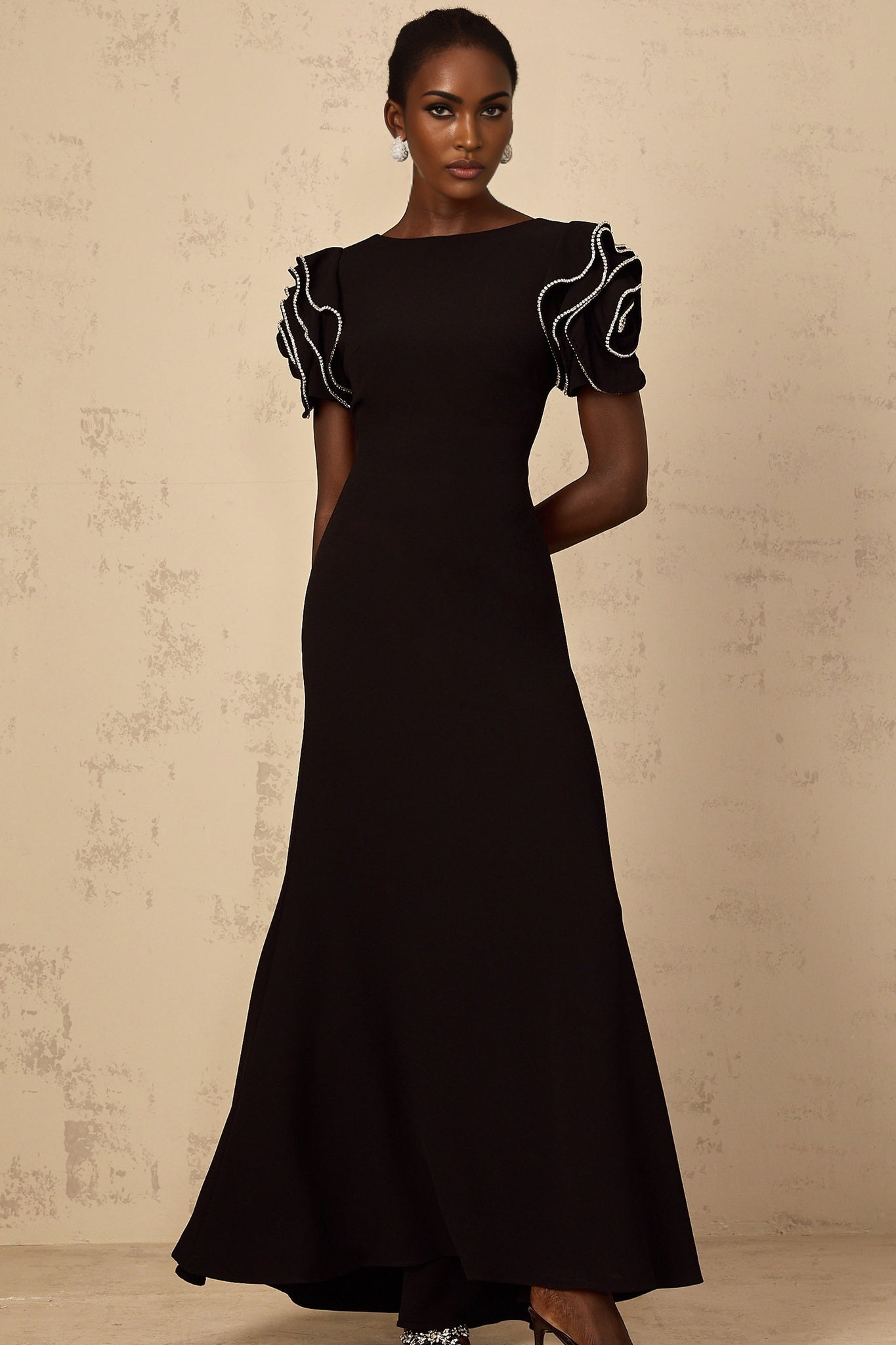 A black maxi dress with ruffled details and embellishments featuring a long flowy silhouette and elegant design by Bruyere