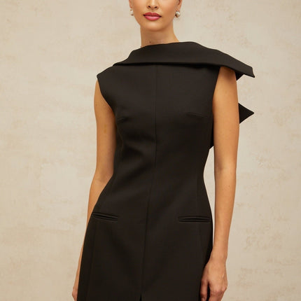 A black midi dress with an open back and deconstructed design worn by a model standing against a plain background