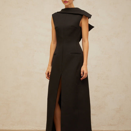 A black midi dress with an open back and deconstructed design worn by a model standing against a plain background