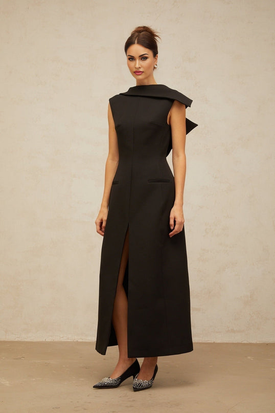 A black midi dress with an open back and deconstructed design worn by a model standing against a plain background
