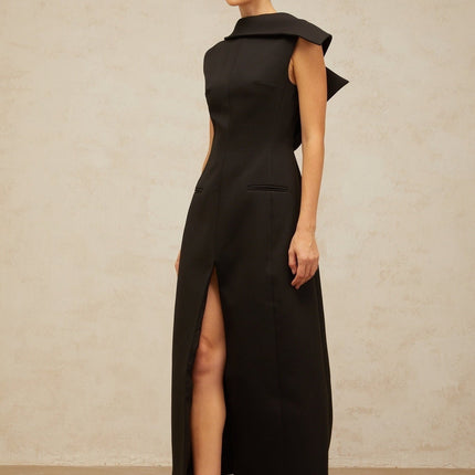 A black midi dress with an open back and deconstructed design worn by a model standing against a plain background