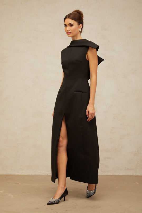A black midi dress with an open back and deconstructed design worn by a model standing against a plain background