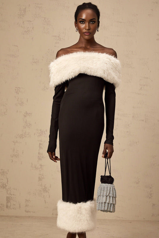 A black midi dress with faux fur trim and an offshoulder neckline worn by a model against a plain background