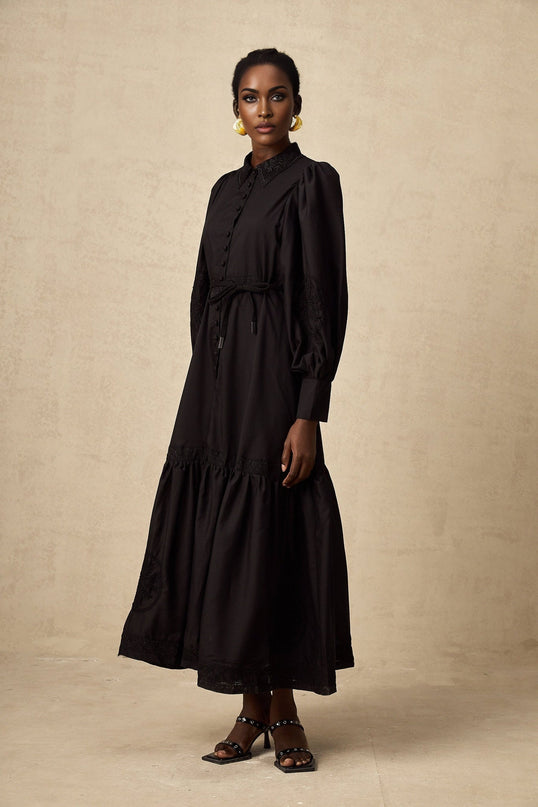 A black midi dress with intricate lace embroidery details styled on a mannequin against a plain background