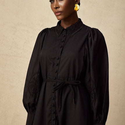 A black midi dress with lace embroidery details covering the bodice and skirt featuring a fitted silhouette and delicate floral patterns