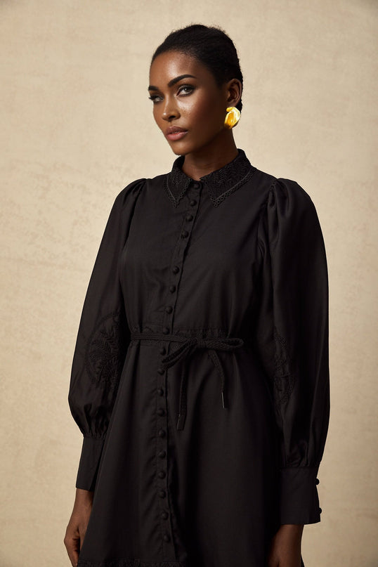 A black midi dress with lace embroidery details covering the bodice and skirt featuring a fitted silhouette and delicate floral patterns