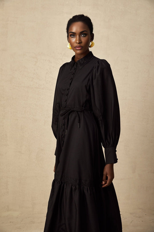 A black midi dress with lace embroidery details featuring a fitted silhouette and delicate floral patterns throughout the fabric