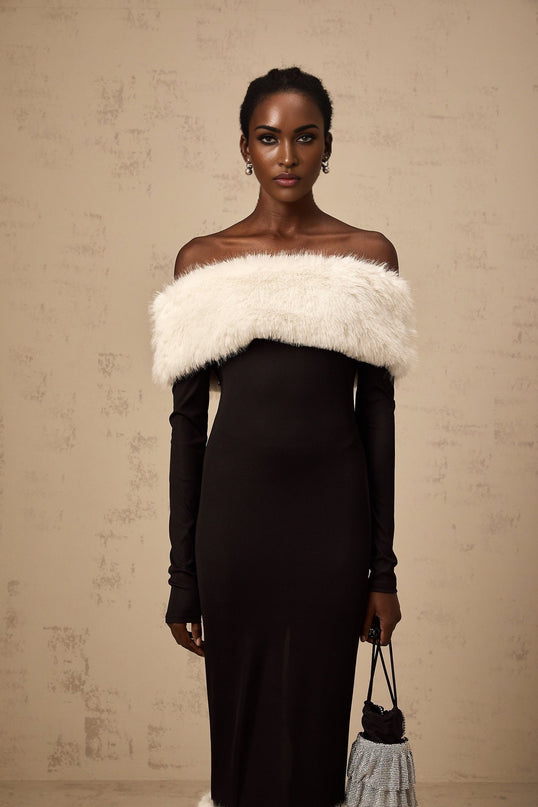 A black midi dress with offshoulder neckline and faux fur trim worn by a model standing against a plain background