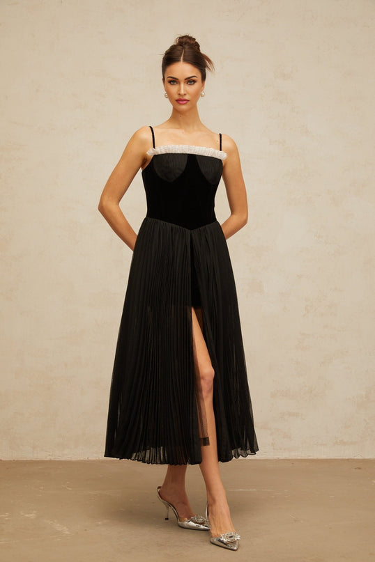 A black midi dress with velvet panels and pleated design featuring long sleeves and a flowy silhouette