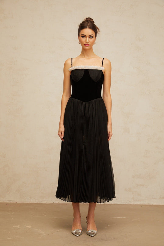 A black midi dress with velvet panels and pleated details featuring a fitted silhouette and long sleeves