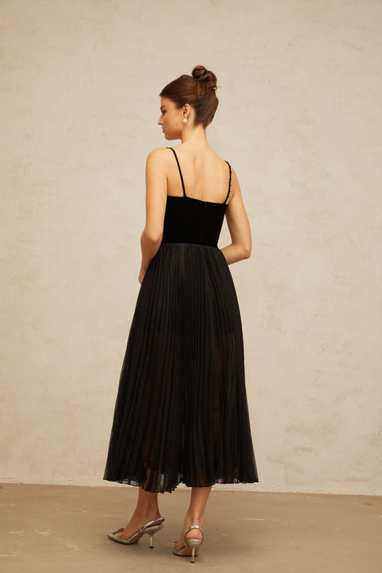 A black midi dress with velvet panels and pleated details featuring long sleeves and a fitted silhouette