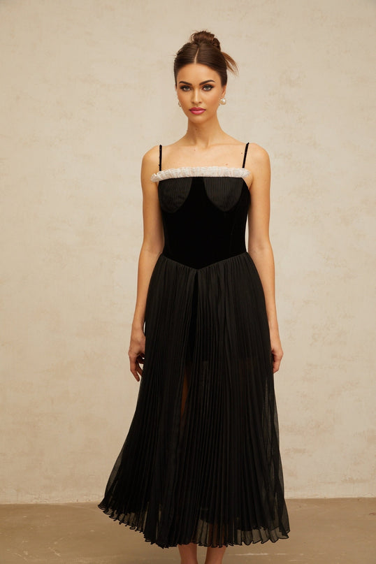 A black midi dress with velvet panels and pleated details featuring long sleeves and a flowing silhouette