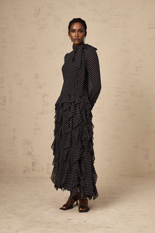 A black midi dress with white polka dots featuring ruffled details and a feminine silhouette called the Coraline dress
