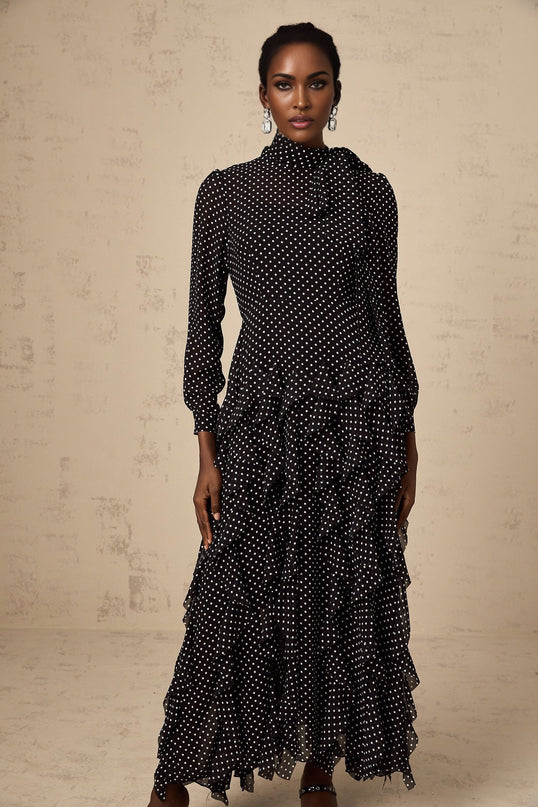 A black midi dress with white polka dots featuring ruffled details and a feminine silhouette named Coraline