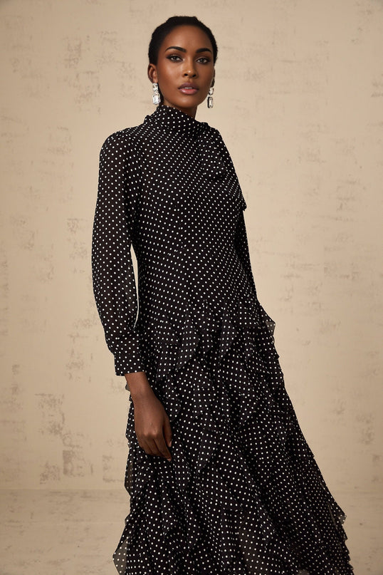 A black midi dress with white polka dots featuring ruffled details and a feminine silhouette named Coraline