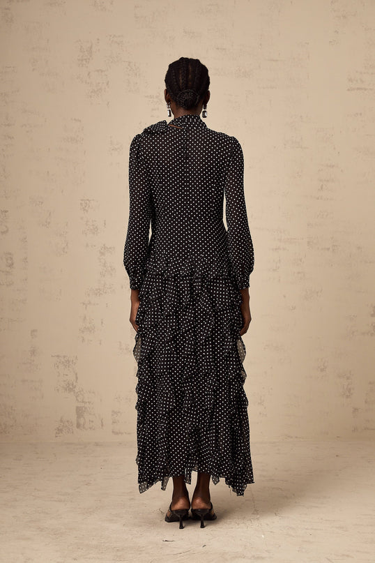 A black midi dress with white polka dots featuring ruffled details and a fitted silhouette named Coraline