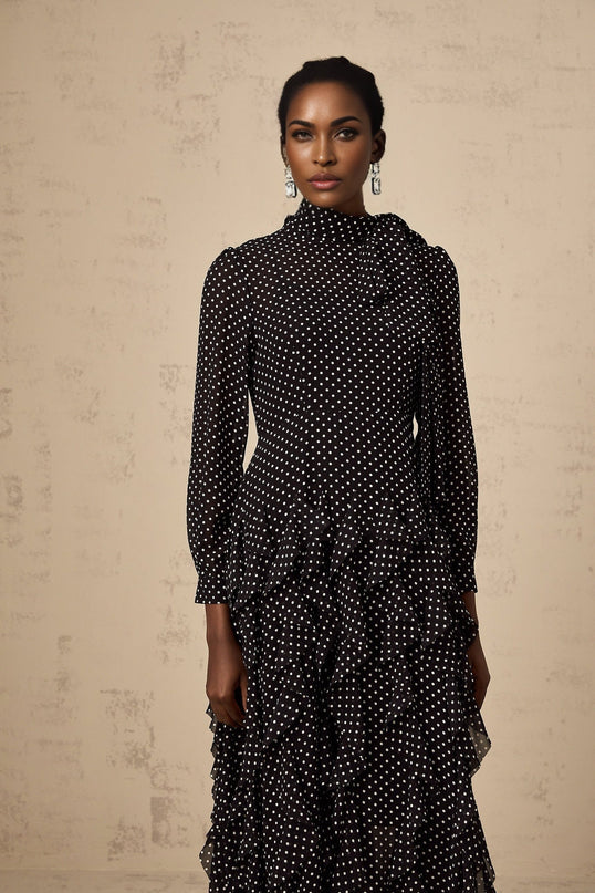 A black midi dress with white polka dots featuring ruffled details and a flowy silhouette named Coraline