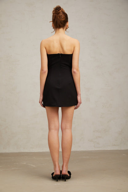 A black mini dress with a fitted silhouette featuring studded details and a decorative bowknot accent