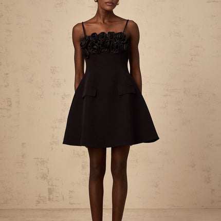 A black mini dress with a flared skirt featuring delicate rose appliqués adorning the fabric The dress has a fitted bodice and short hemline creating a feminine silhouette