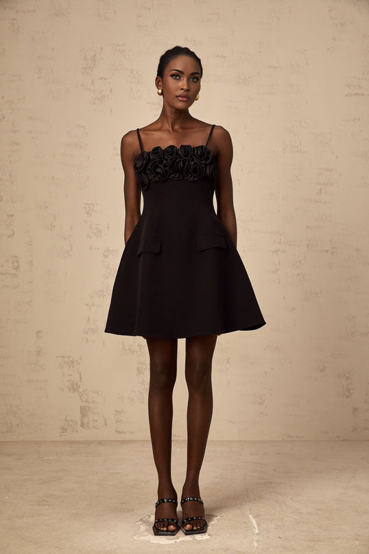 A black mini dress with a flared skirt featuring delicate rose appliqués adorning the fabric The dress has a fitted bodice and short hemline creating a feminine silhouette
