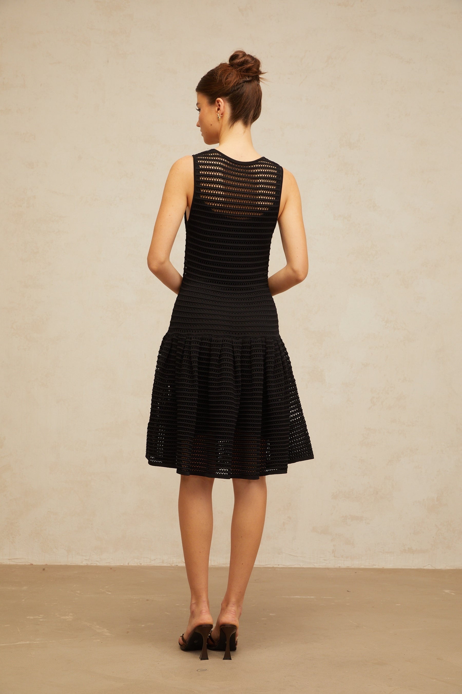 A black mini dress with a flounced hem and pointelle knit pattern featuring a fitted silhouette and short sleeves