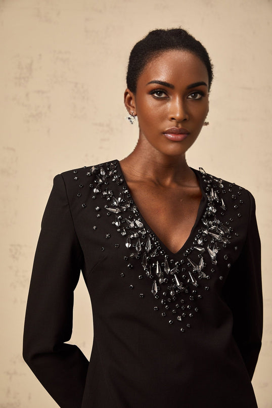 A black mini dress with a plunging V neckline adorned with crystal embellishments featuring a formfitting silhouette and short hemline