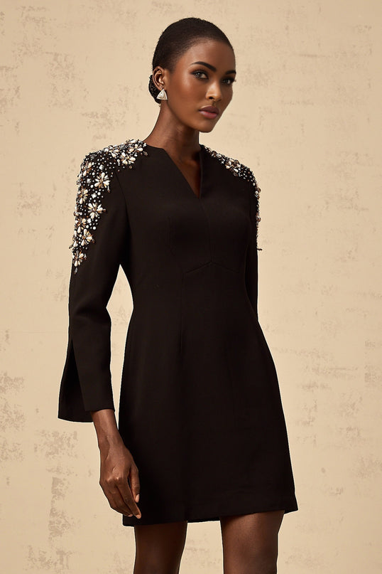 A black mini dress with a split neckline and embellished details worn by a model against a plain background