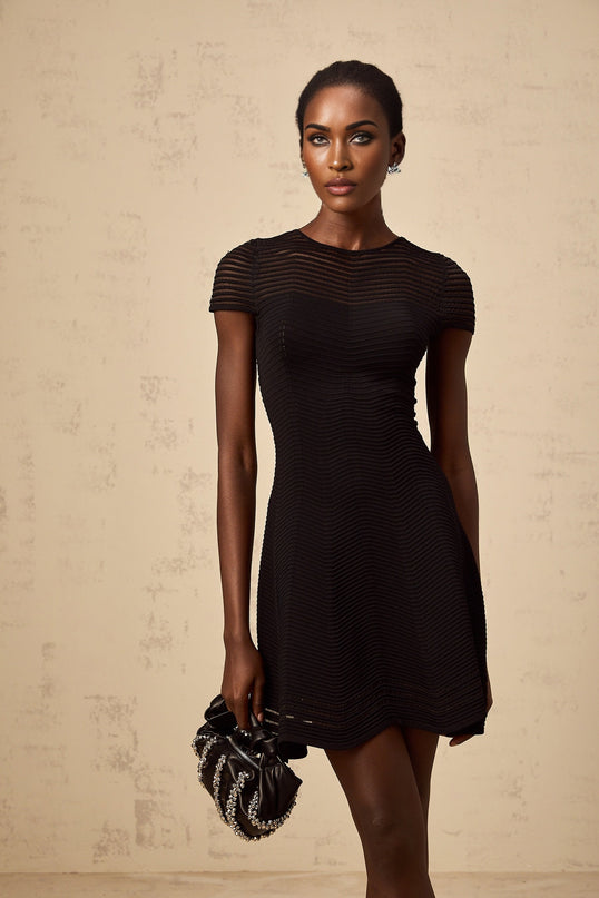 A black mini dress with a wavy crochet texture worn by a model standing against a plain background