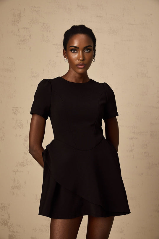 A black mini dress with an asymmetric design featuring ruffles worn by a model named Emma