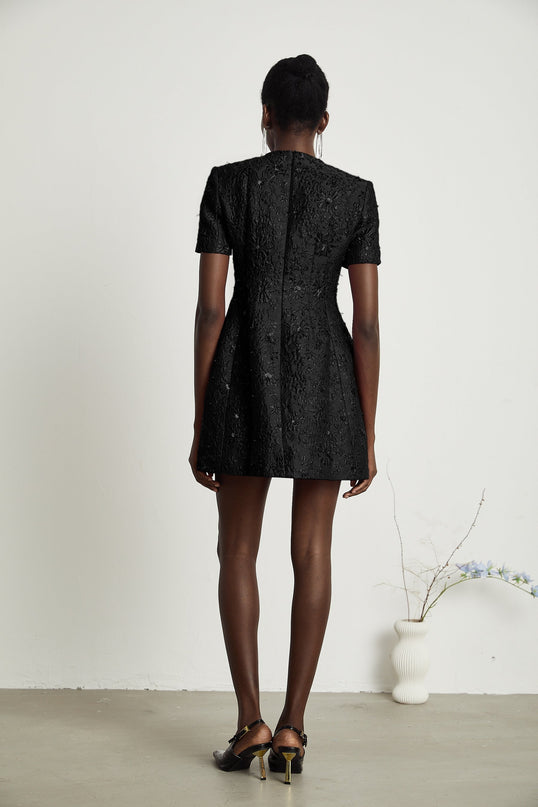 A black mini dress with floral applique embellishments and a short hemline