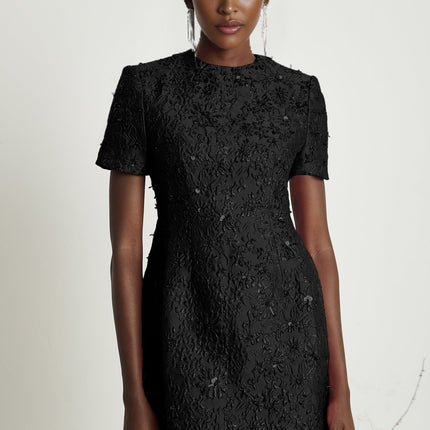 A black mini dress with floral applique embellishments featuring a short hemline and intricate flower details adorning the fabric
