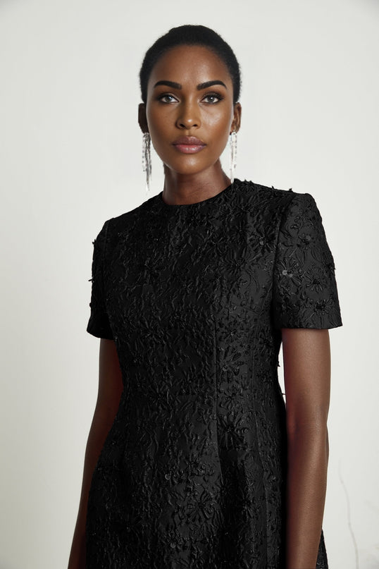 A black mini dress with floral applique embellishments featuring a short length and decorative flower designs on the fabric