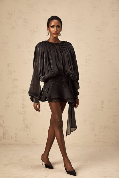 A black mini dress with full pleats and ruffled details featuring a short hemline and feminine silhouette