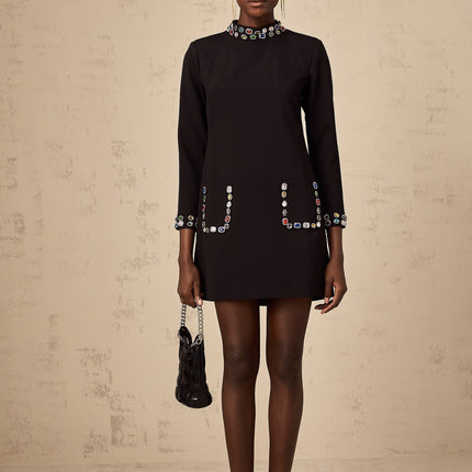 A black mini dress with long sleeves featuring crystal embellishments worn by a model against a plain background