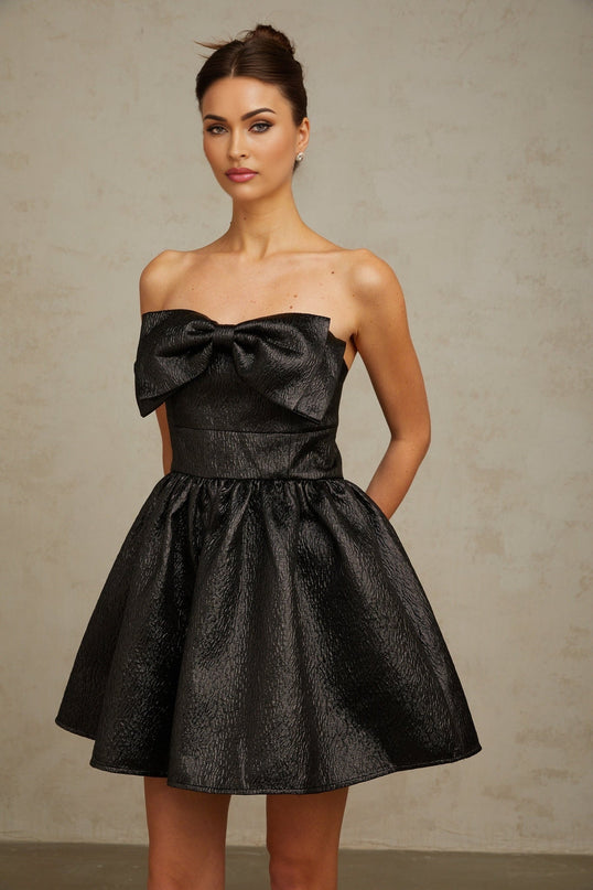 A black mini dress with metallic accents and a bow detail named Colette