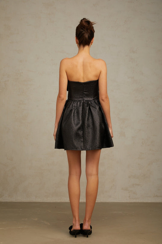 A black mini dress with metallic accents and a decorative bow detail named Colette