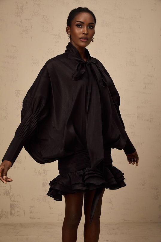 A black mini dress with ruffled details and a pussy bow neckline worn by a model named Melanie