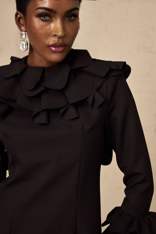 A black mini dress with ruffled details and an open back design called the Jacques dress