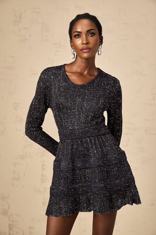 A black mini dress with sequin embellishments and a knitted texture worn by a model against a plain background