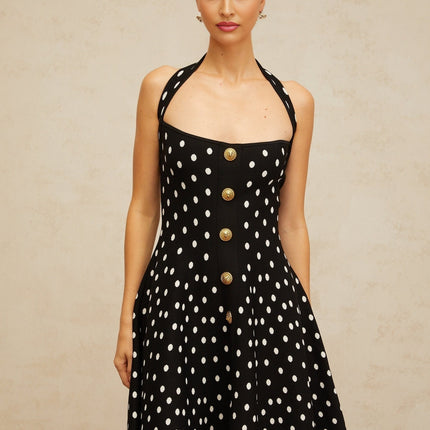 A black mini dress with white polka dots and a knit texture worn by a model against a plain background