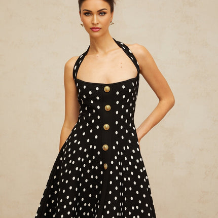 A black mini dress with white polka dots and a knit texture worn by a model standing against a plain background