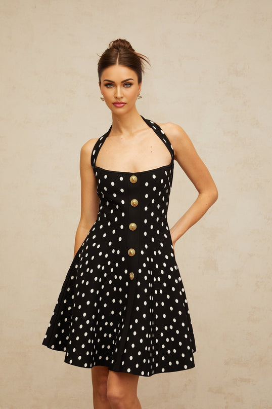 A black mini dress with white polka dots and a knit texture worn by a model standing against a plain background