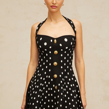 A black mini dress with white polka dots and a knit texture worn by a model standing against a plain background