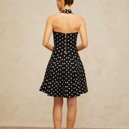A black mini dress with white polka dots made of knit fabric featuring a fitted silhouette and short length