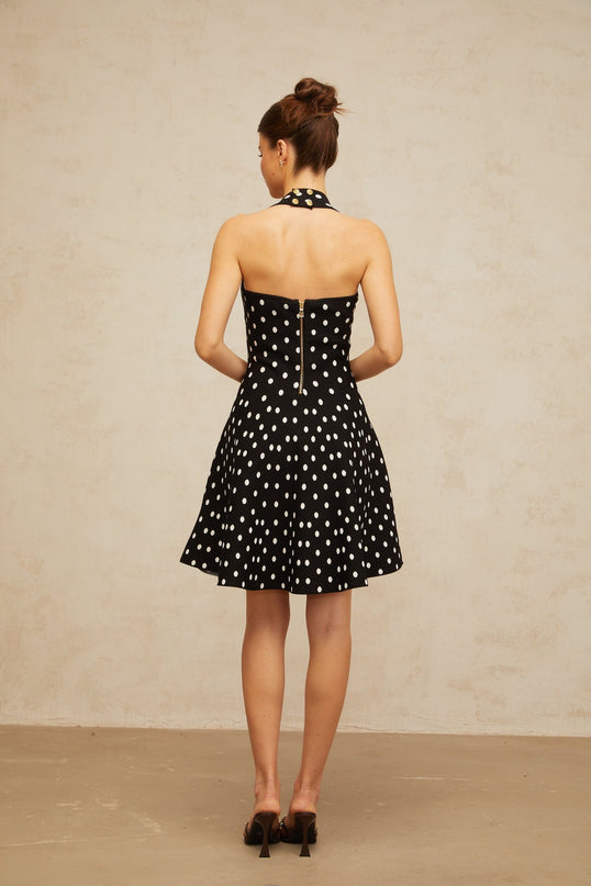 A black mini dress with white polka dots made of knit fabric featuring a fitted silhouette and short length