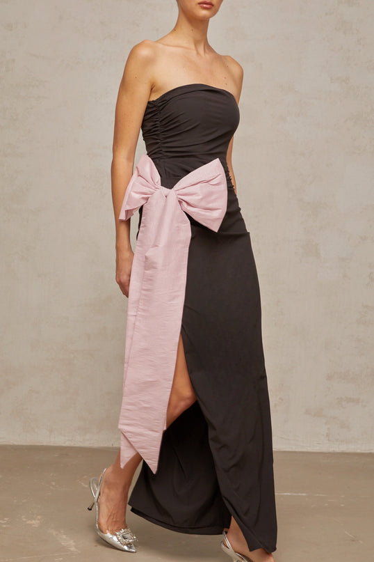 A black off shoulder maxi dress with a bowknot detail worn by a model standing against a plain background