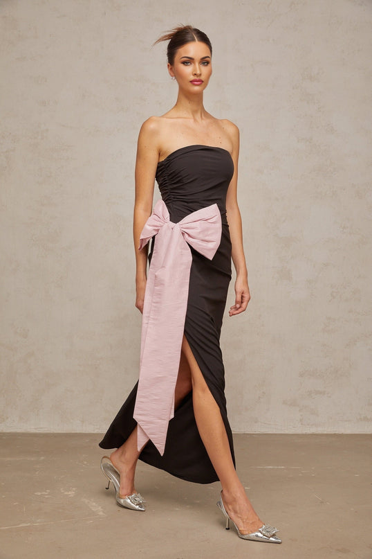 A black offshoulder maxi dress with a bow detail worn by a model standing against a plain background
